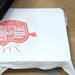 Completed red Enjoy the Ride guitar transfer on a white shirt resting on the table of the Digital Knight DK20S