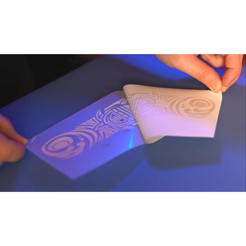 Hands peeling a white toner transfer carrier sheet with tribal artwork, part of the UNINET White Toner Training Program demonstrations